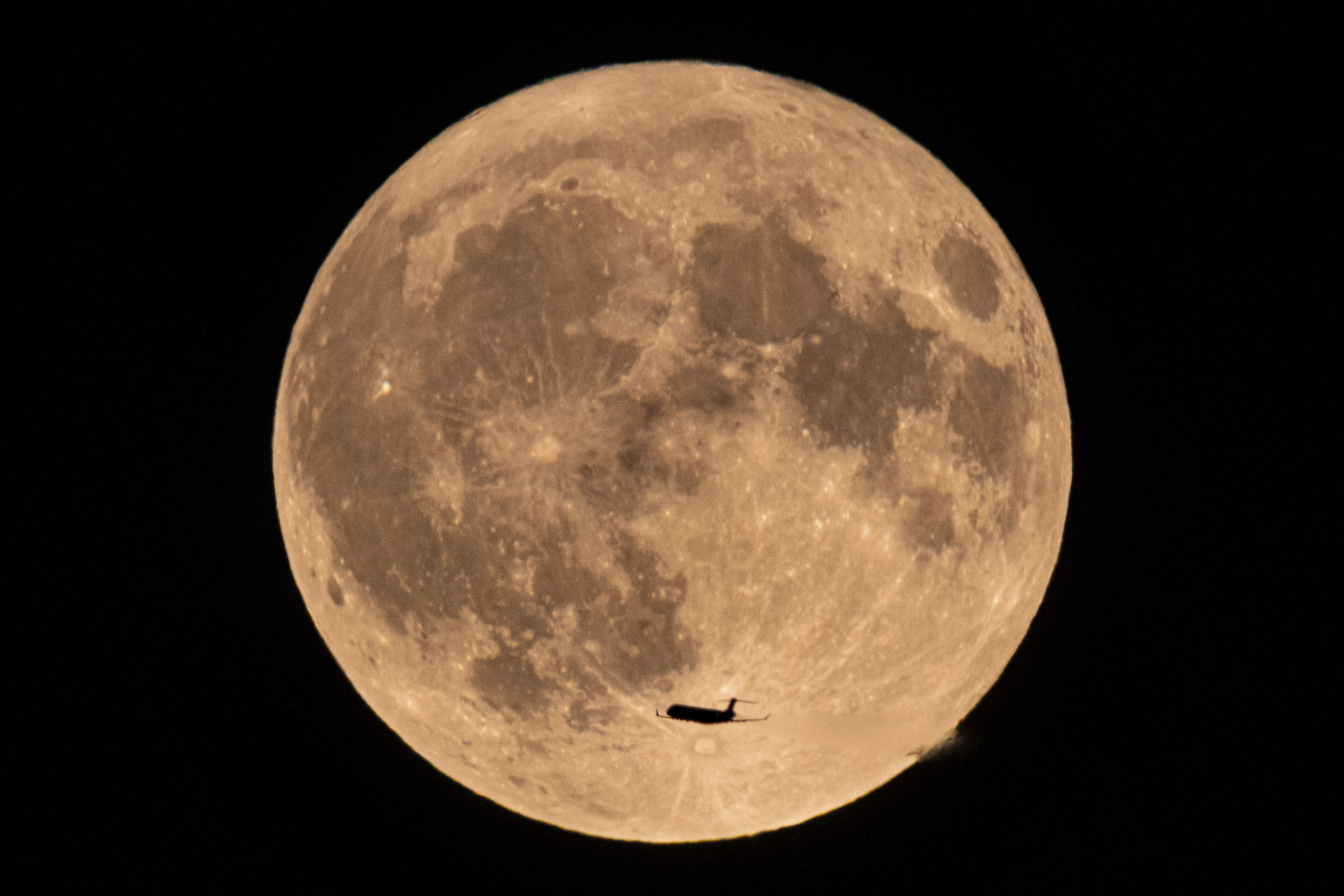 An image of a yellowish, near-full moon with an airplane silhouetted flying in its lower half.