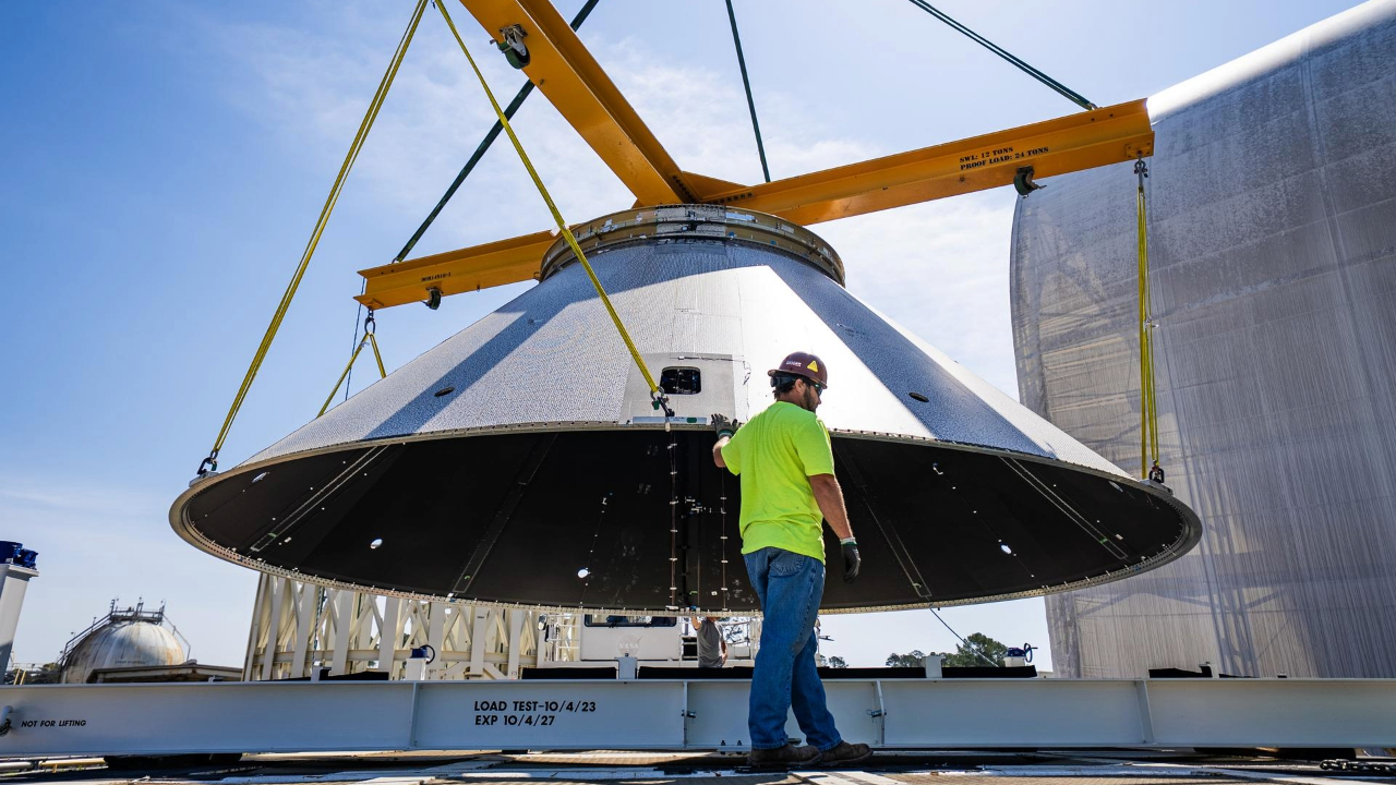 A man in a bright shirt and hard hat stands next to a domed piece of metal on a crane