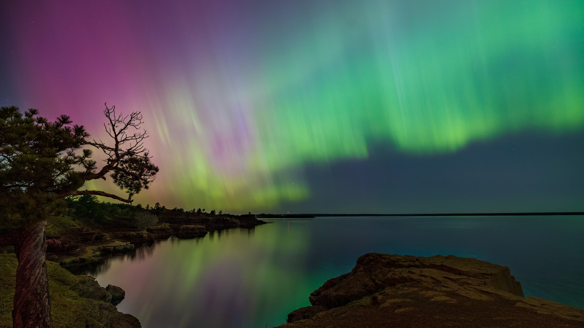 colorful green wisps of light dance in the sky above a lake, which reflects them