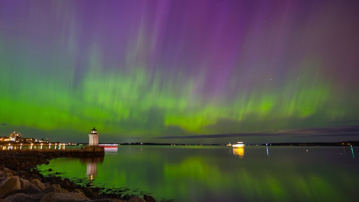sky above maine is filled with northern lights, ribbons of green and purple fill the sky.