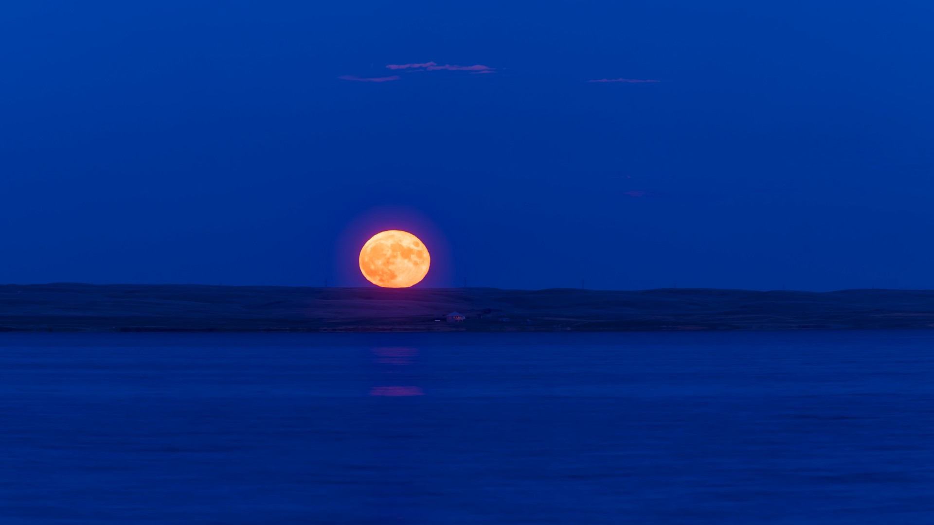 A yellow-tinged full moon is pictured rising above a coastal landscape at night.