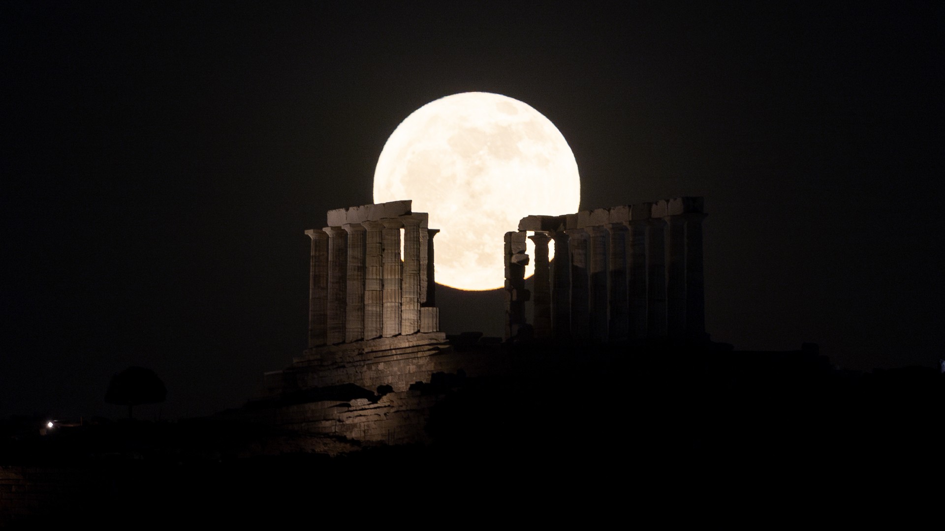 a bright white full moon rises above the ruins of an ancient building
