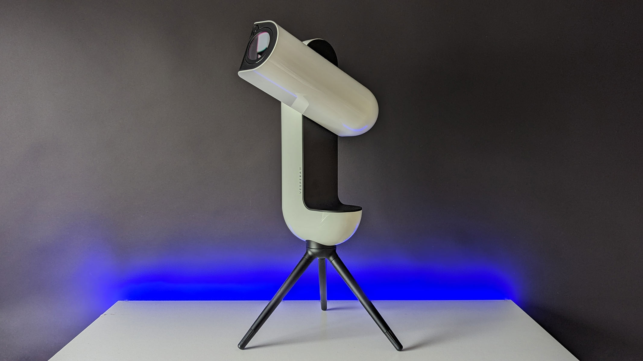 The Vaonis Vespera II smart telescope on a white tabletop with the optical tube assembly pointing upwards.