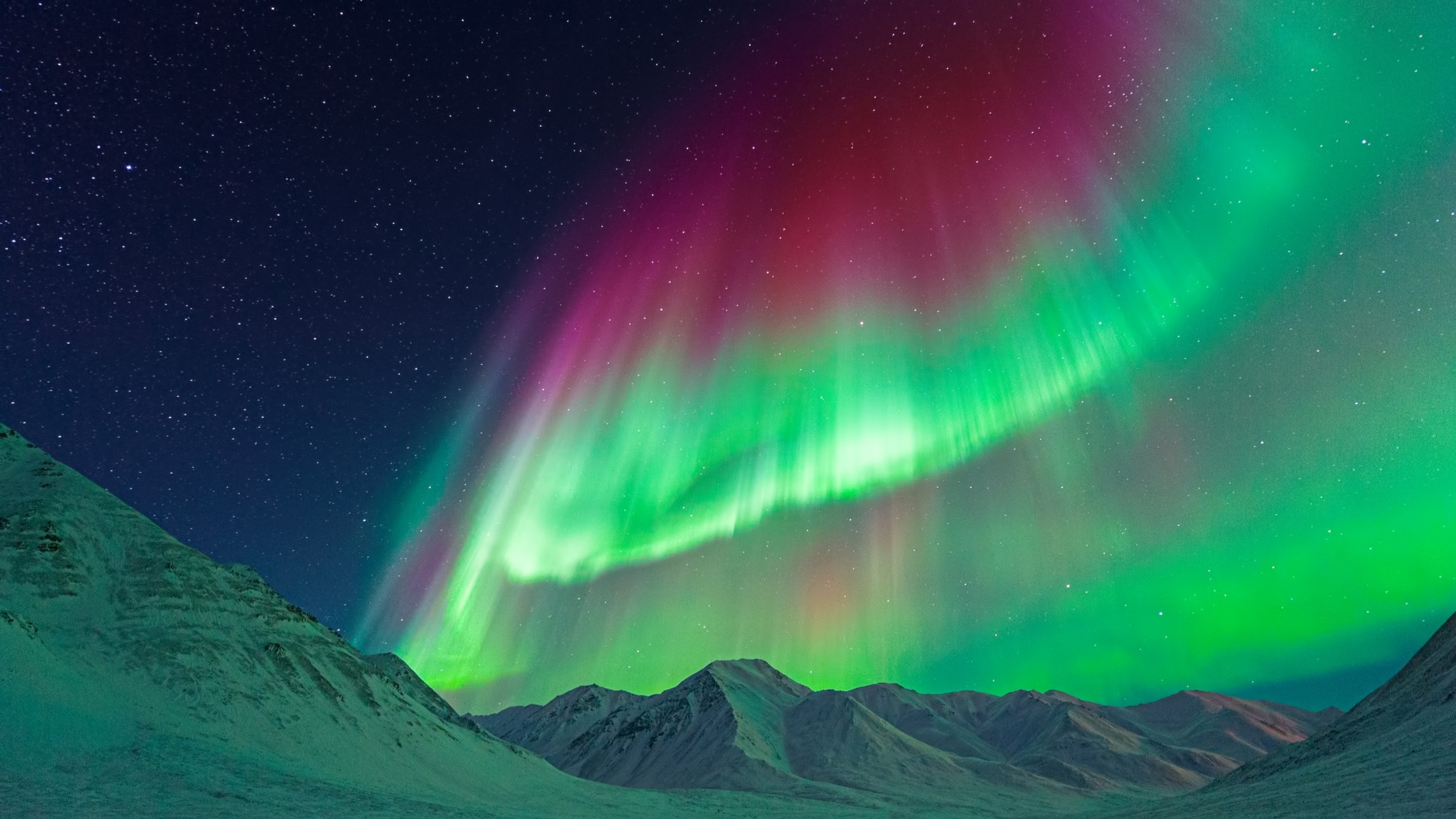 Gigantic Aurora borealis (Northern Lights) above mountains near Atigun Pass, Dalton Highway, Alaska, USA. auroras appear as ribbons of green and pink light dancing across the sky.