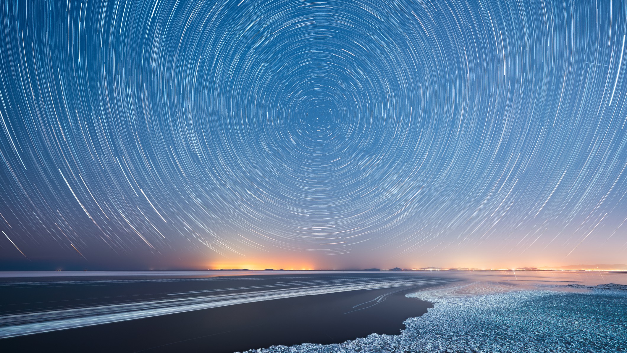 A long exposure camera shot in which startrails are captured circling the north star polaris above a beach in China.