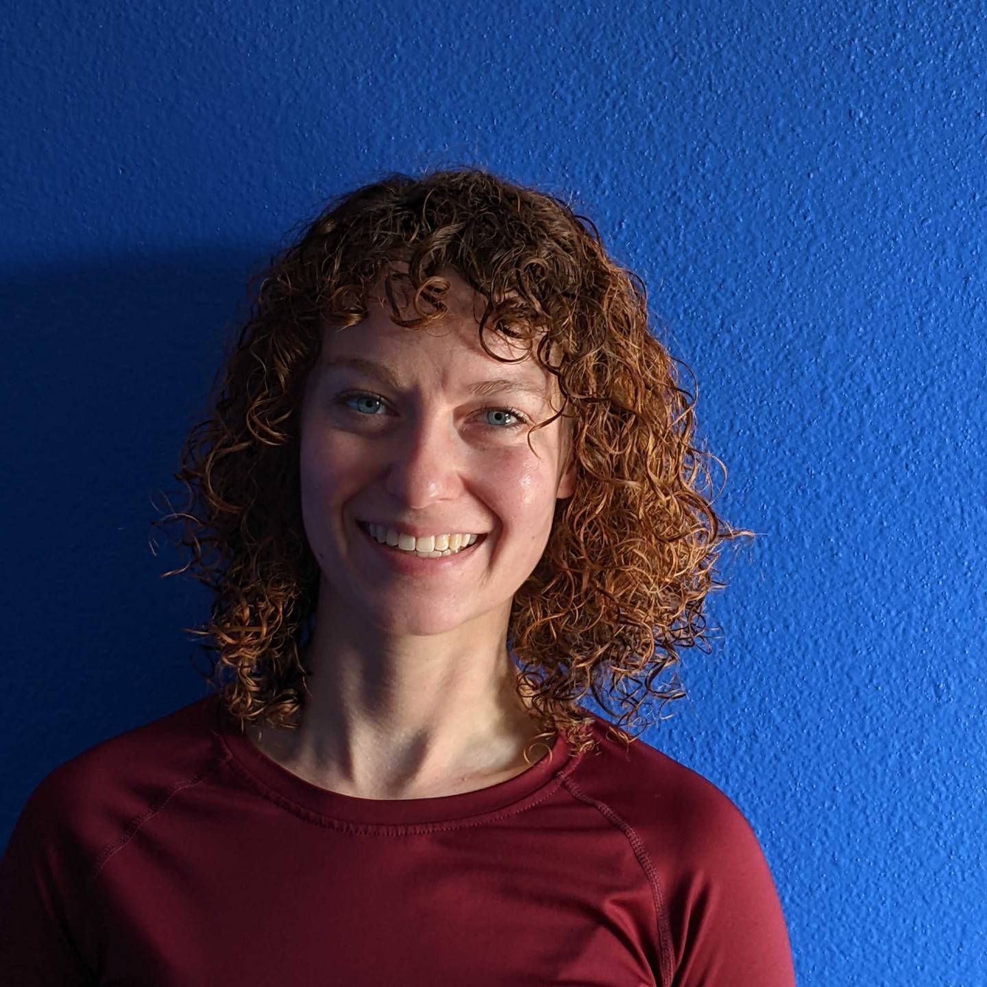 a woman with curly hair smiles for a portrait in front of a stucco wall