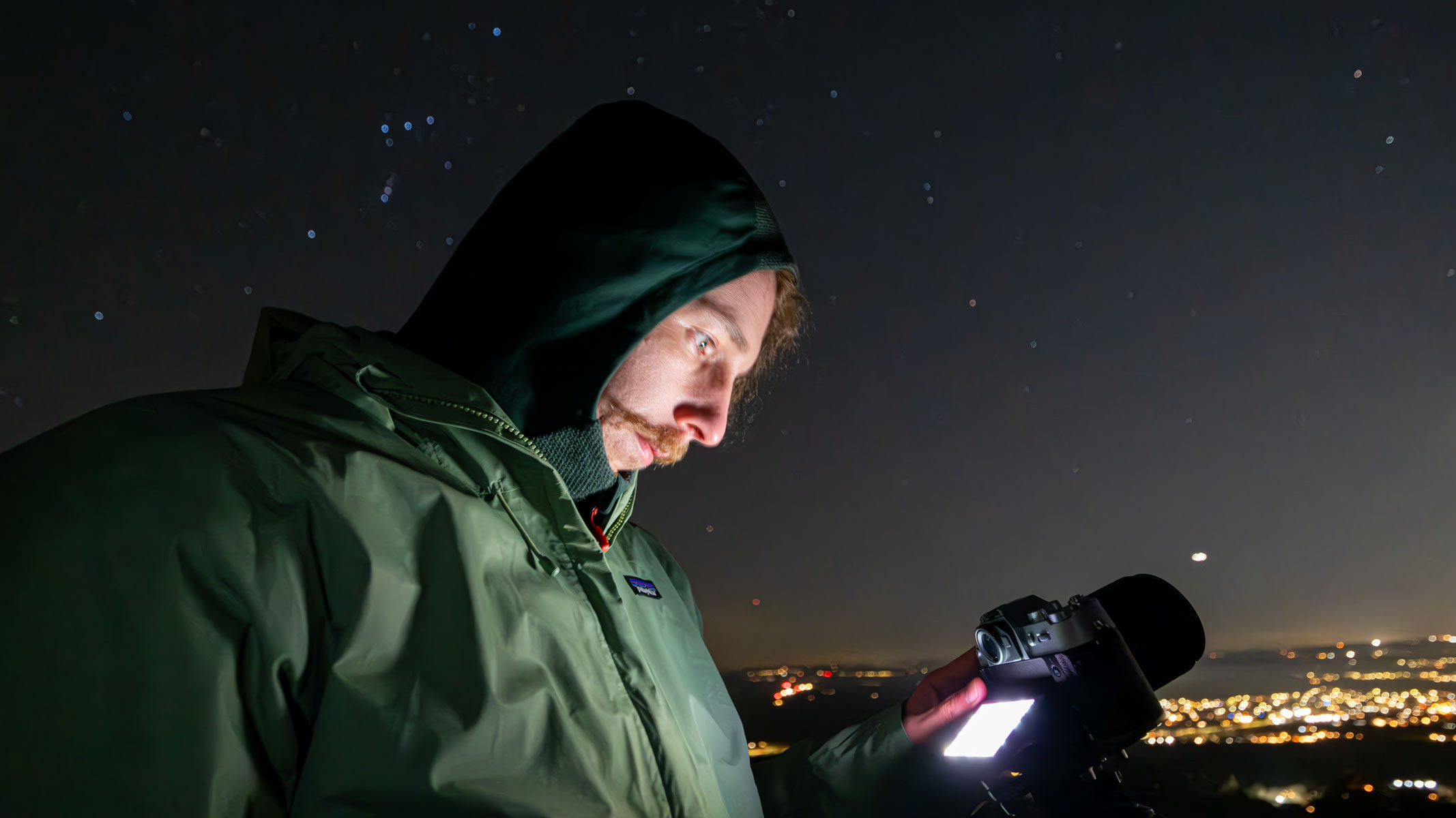 A man looking down at a Fujifilm X-T50 with stars and streetlights in the background.